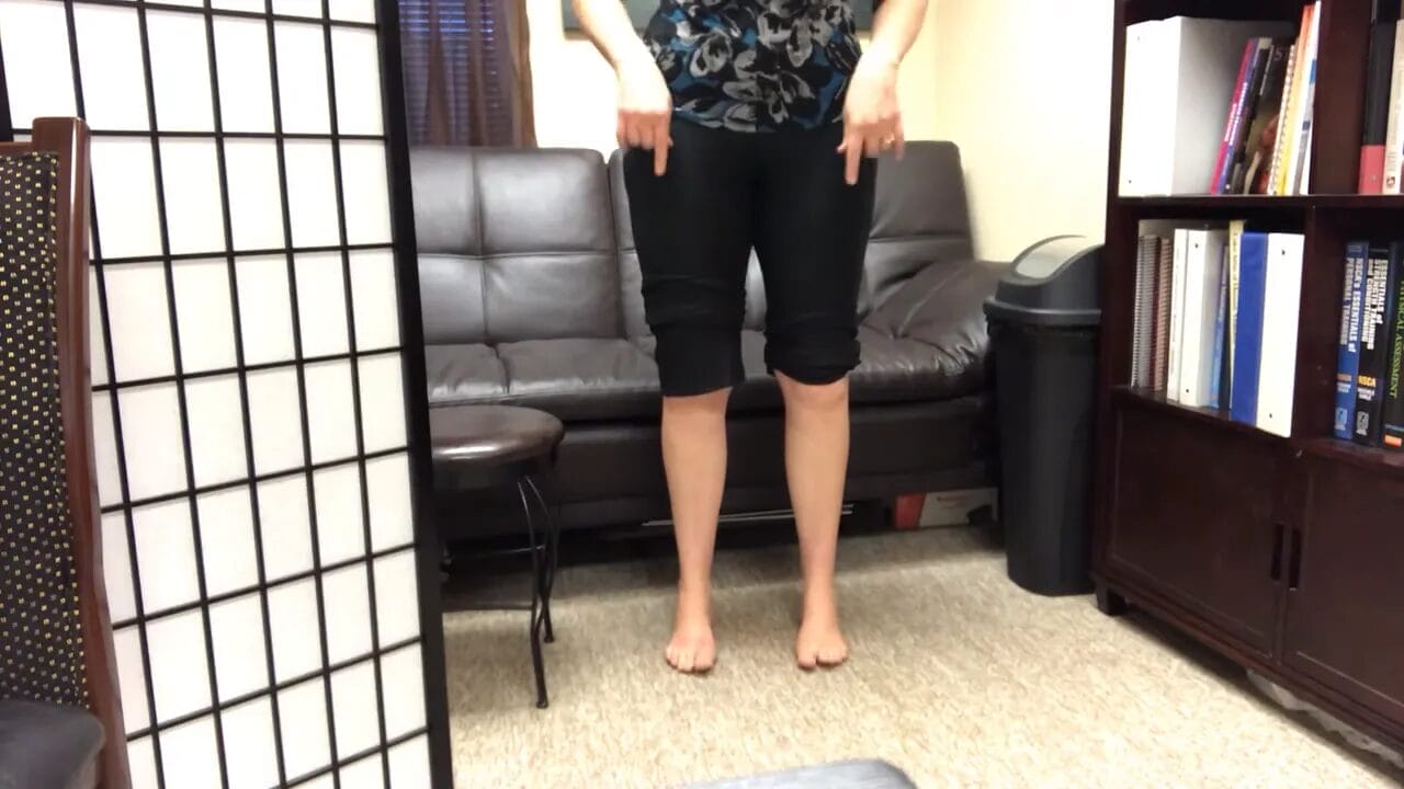Person standing barefoot pointing down at their lower legs (shanks) to indicate shank rotation